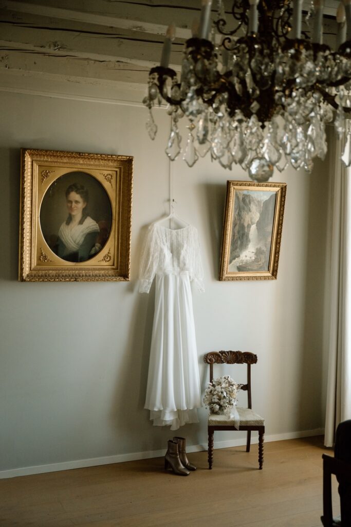 Lace wedding dress hanging beneath a crystal chandelier in a vintage room
