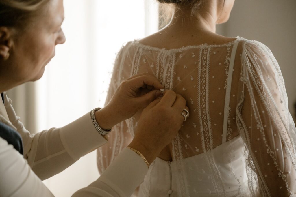 Detail of lace wedding dress back buttons being fastened by the mother of the bride
