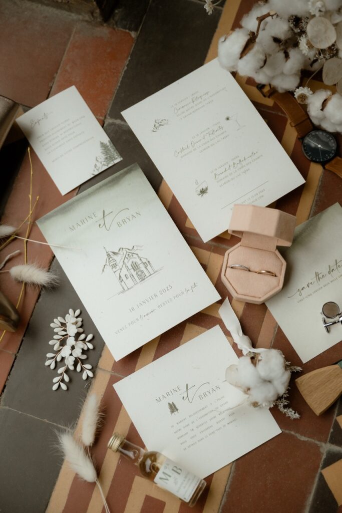 Flat lay of wedding stationery, rings and dried cotton flowers for a winter wedding at Lake Annecy
